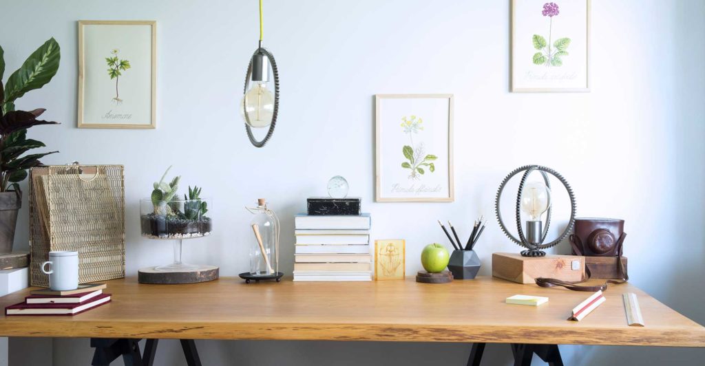 Wooden office desk with books and quirky desk decor on top along with flower illustrations hung up on the wall.