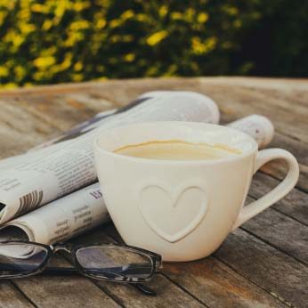 Newspaper, reading glasses and a cup of coffee on a wooden table, outdoors.
